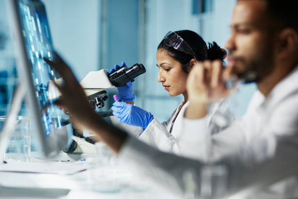 Two researchers in lab coats examining microscopes while studying mecfs.