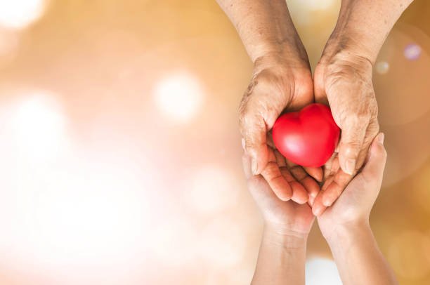 Two hands holding a red heart on a background symbolizing love and compassion, emphasizing the significance of mecfs awareness.